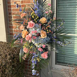 Tall standing floral spray with pink and peach roses and blue flowers