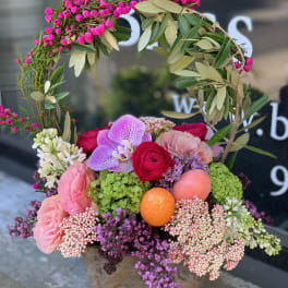 Pink and purple floral arrangement in a stone pot with a leafy wreath handle