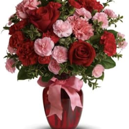 Red roses and red and pink carnations in a red glass vase with a pink bow