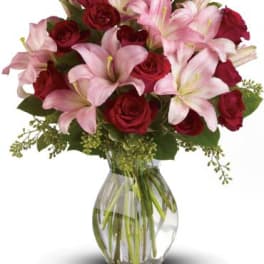 Arrangement of pink lilies and red roses in a clear glass vase with water.