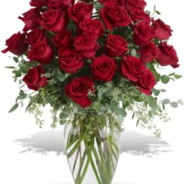 Red roses arranged in a clear glass vase with greenery