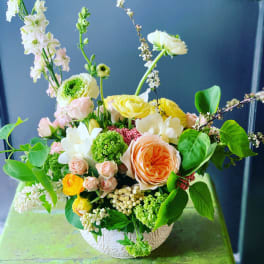 Mixed bouquet in a patterned bowl vase with peach, yellow, white, and green blooms
