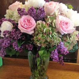Pink roses and white blooms arranged in a clear glass vase with purple flowers