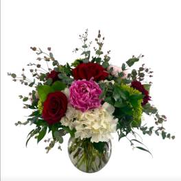 Bouquet of red roses, pink peonies, and white hydrangeas in a glass vase