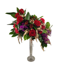 Red roses and purple flowers in a tall clear glass vase