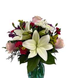 Bouquet of white lilies, pink roses, and mixed blooms in a blue glass vase