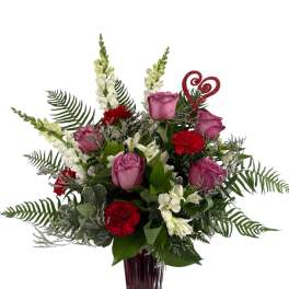 Pink roses and red carnations in a tall burgundy vase with a glitter heart pick