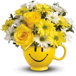 Yellow roses and white and yellow daisies arranged in a yellow smiley-face mug