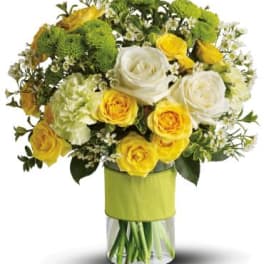 Yellow and white roses in a glass vase with green blooms