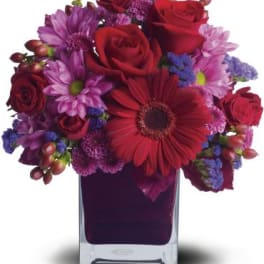 Red roses and purple daisies in a clear square vase
