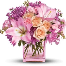 Pink lilies, roses, carnations, and mums arranged in a pink rectangular glass vase