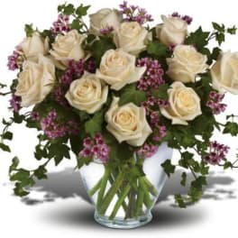 Cream roses with purple filler flowers in a clear glass vase