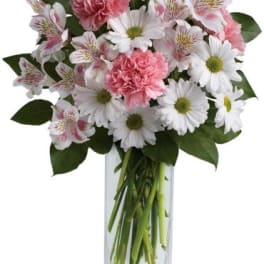 Tall bouquet of white daisies, pink carnations, and white alstroemeria in a clear rectangular glass vase