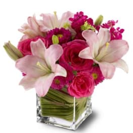 Pink lilies and roses arranged in a clear square vase