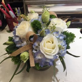 White roses and blue hydrangeas in a glass vase with burlap ribbon