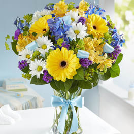 Bouquet of yellow gerbera daisies, white daisies, and blue flowers in a glass vase