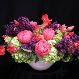 Pink peonies and purple lilacs arranged in a white bowl vase