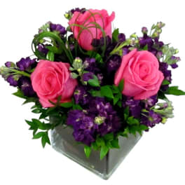 Pink roses and purple flowers in a clear square vase