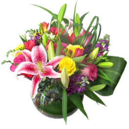 Mixed bouquet with pink lilies, yellow roses, and purple flowers in a glass vase