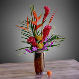 Tropical flower arrangement in a tall metallic vase with a small candle nearby