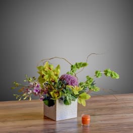Tropical floral arrangement in a white textured cube vase with a small orange candle nearby