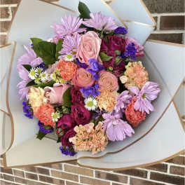 Mixed bouquet of pink, purple, and peach flowers wrapped in pale paper