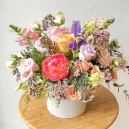 Mixed pastel flower arrangement in a white vase on a wooden stool