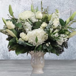 White floral arrangement in a beige vase with lilies, roses, and hydrangeas