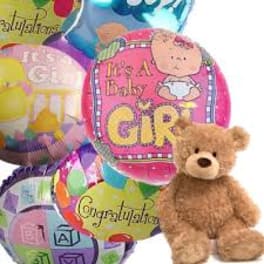 Cluster of baby girl themed foil balloons with a brown teddy bear in front