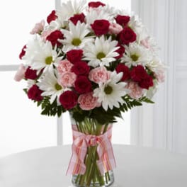 Bouquet of red roses, pink carnations, and white daisies in a glass vase