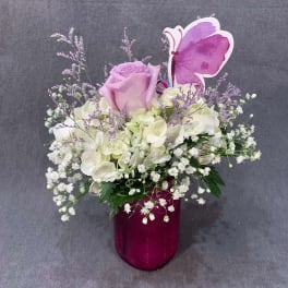 Lavender rose and white hydrangea arrangement in a magenta vase with a butterfly pick