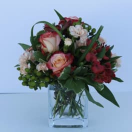 Short bouquet of red and blush roses with accent blooms in a clear square glass vase
