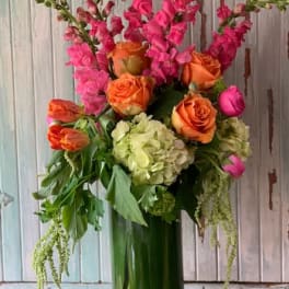 Orange roses and pink snapdragons in a tall glass vase