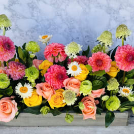 Rectangular floral arrangement with pink, yellow, and green blooms in a low container