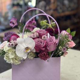 Pink and white floral arrangement in a lavender gift bag