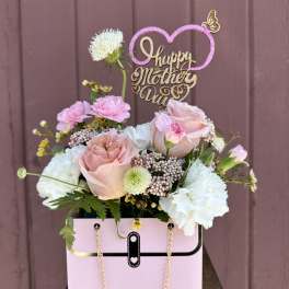 Pink and white floral arrangement in a pink handbag box with a "Happy Mother's Day" topper