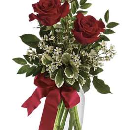 Red roses in a clear glass vase with a burgundy ribbon
