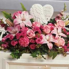 Pink lilies and roses arranged with angel wings and a heart plaque