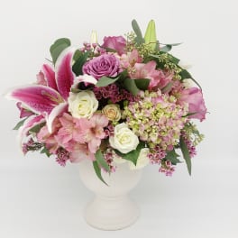 Pink and white mixed flower arrangement with lilies and roses in a white urn-style vase
