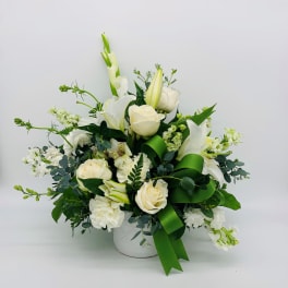 White flower arrangement with roses and lilies in a white vase with a green ribbon bow