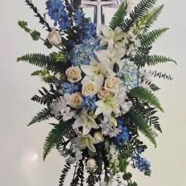Standing floral spray with white lilies, blue flowers, and a cross