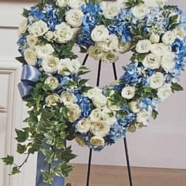 Heart-shaped floral wreath with white roses and blue hydrangeas on a stand