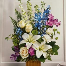 Tall floral arrangement with white lilies, cream roses, blue delphinium, and purple alstroemeria