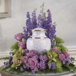 Purple floral arrangement around a white urn vase