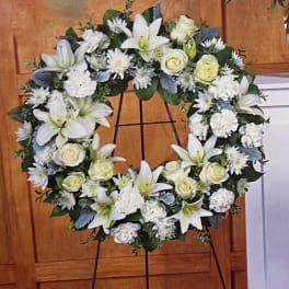 White floral wreath on a black stand with lilies and roses