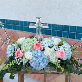 Floral arrangement with roses and hydrangeas around a clear glass cross