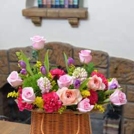 Basket arrangement of pink and peach roses with purple tulips and carnations