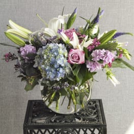 Mixed bouquet in a clear glass vase with lilies, roses, and hydrangeas