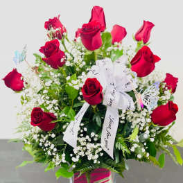 Red roses arranged in a clear square vase with white baby's breath and a white ribbon