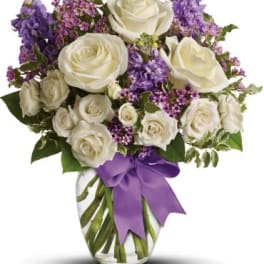 White roses and purple flowers in a glass vase with a purple ribbon
